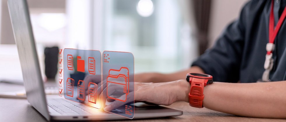 Eine Frau mit roter Armbanduhr tippt auf einem Laptop. Über Ihren Händen schweben Computer-Symbole und Icon.