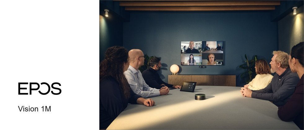 In einem Meetingraum sitzen 6 Personen an einem Tisch. Am Ende ist ein Monitor und darunter die VSION 1M Kamera von EPOS.