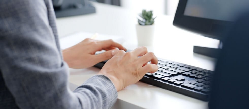 Detailansicht auf die Hände einer Person, die an einer Computertastatur arbeitet